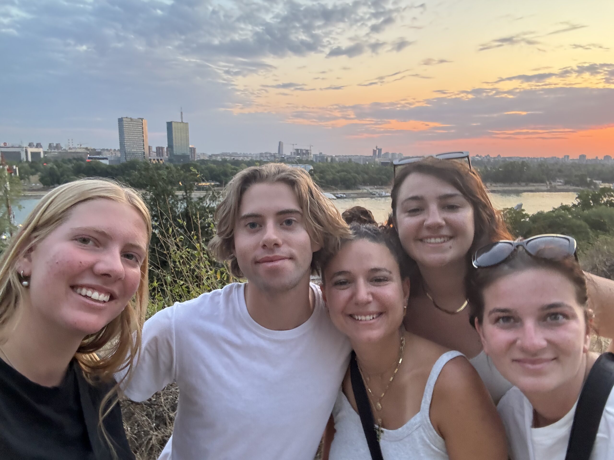 Three women and one man smiling in front of Belgrade sunset while staying in hostels