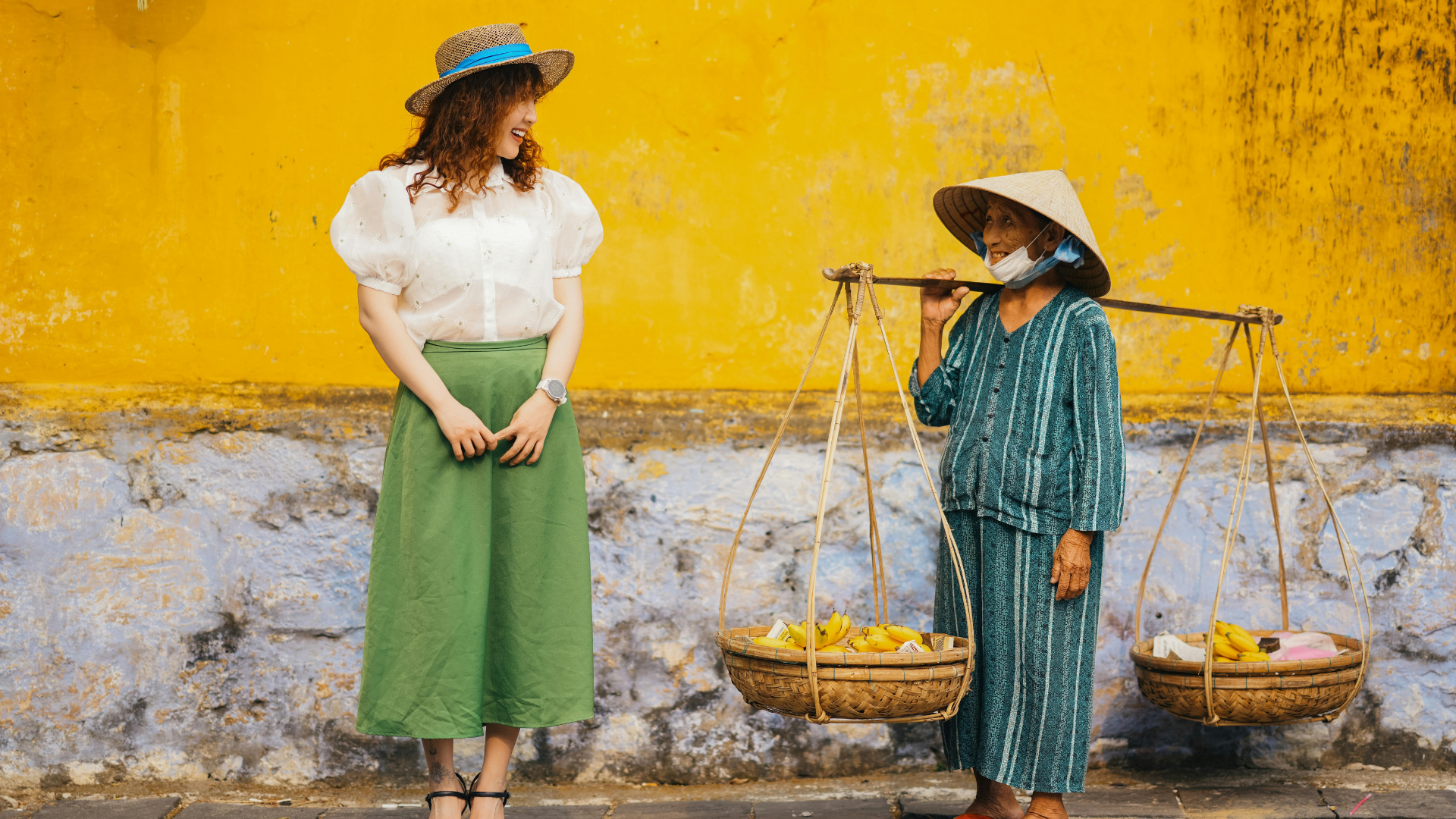 Local woman with rice hat and baskets smiling at woman in green pants